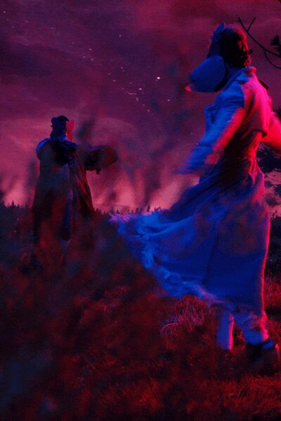 White high-neck dress with tiered ruffles lifting in the wind. Structured white hood jutting forward from the face. White socks pulled above the ankle. Black strap shoes with a thick, rounded sole. Dusk in a field, mid-turn while the bonfire smoke starts to drift.