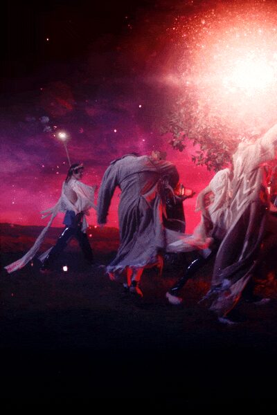 Long dove-grey tunic in crinkled gauze, dragging into streamers at the hem. Dark glossy leggings catching the light at the shin. Red heels flashing under the torn hem. Running across wet grass toward the bonfire after midnight.