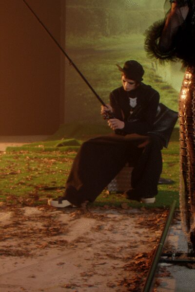 Black felt cloche with a narrow downturned brim. Black draped top over a white chest insert. Floor-sweeping black trousers pooling over the shoes. Two-tone spectator shoes with pale vamp panels. By the fake pond after midnight, fishing line slack in one hand.