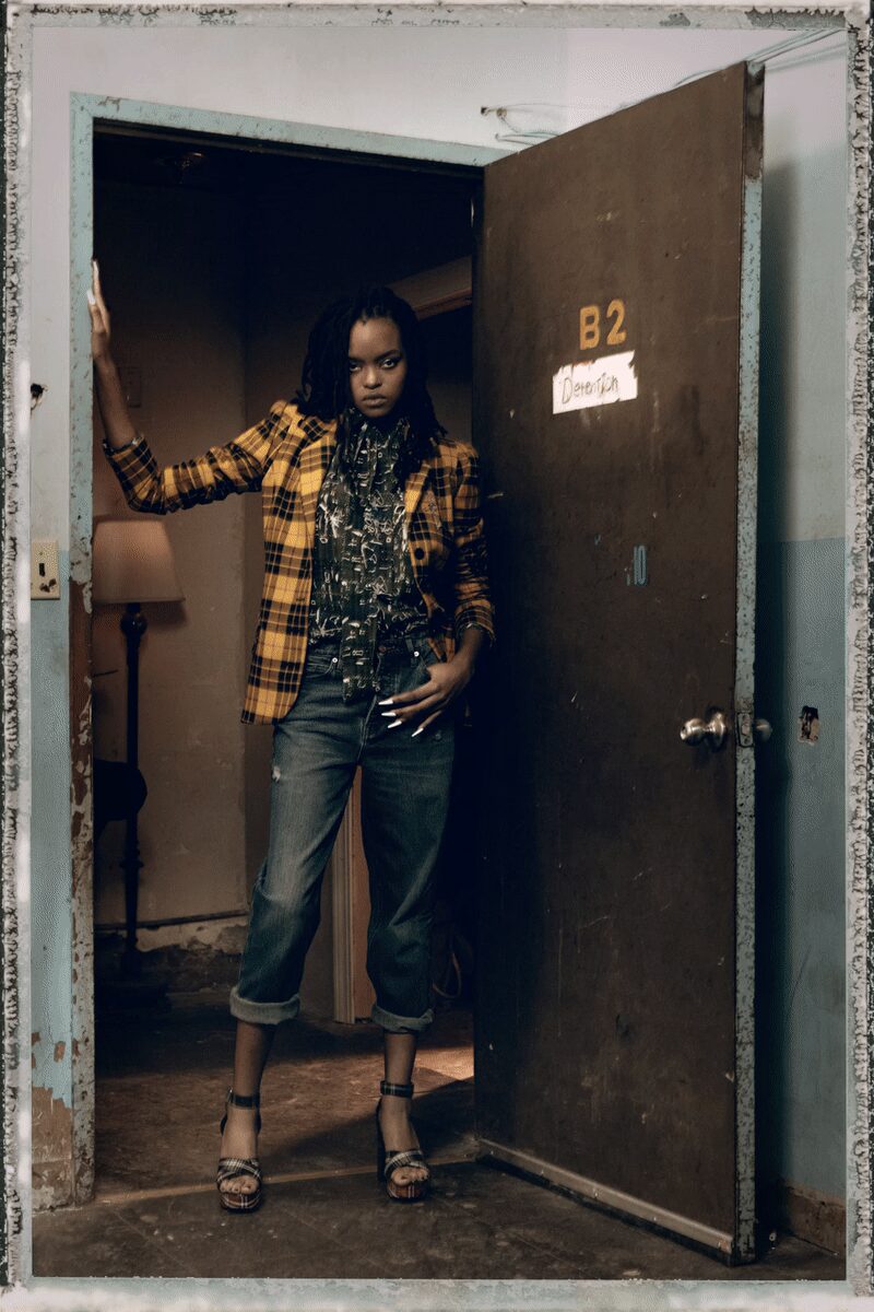 Ochre and black plaid blazer, sleeves pushed and waist lightly nipped. Inky sheer blouse crowded with tiny white motifs and a long neck tie. Faded blue jeans, straight and cuffed high above the ankle. Snakeskin platform sandals with slim black ankle straps. Answering the motel door when you already know who it is.
