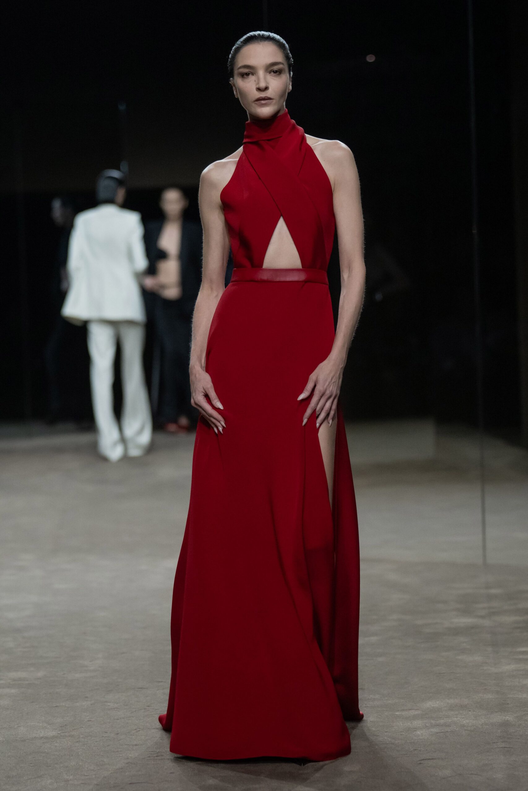 Scarlet column gown with crossed halter bands, a sheer waistband and thigh slit. For arriving at a benefit after the string quartet has already started.